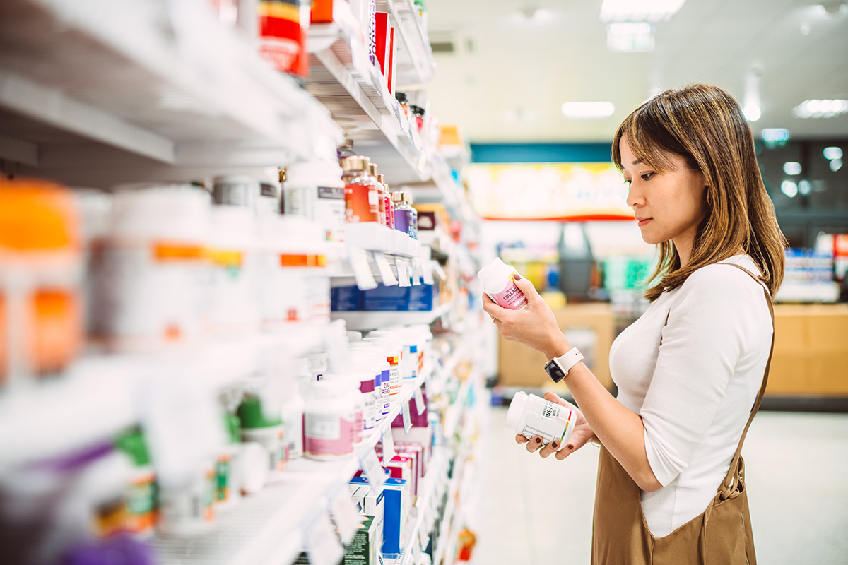 A woman examines a pill bottle in the aisle of a supermarket.
