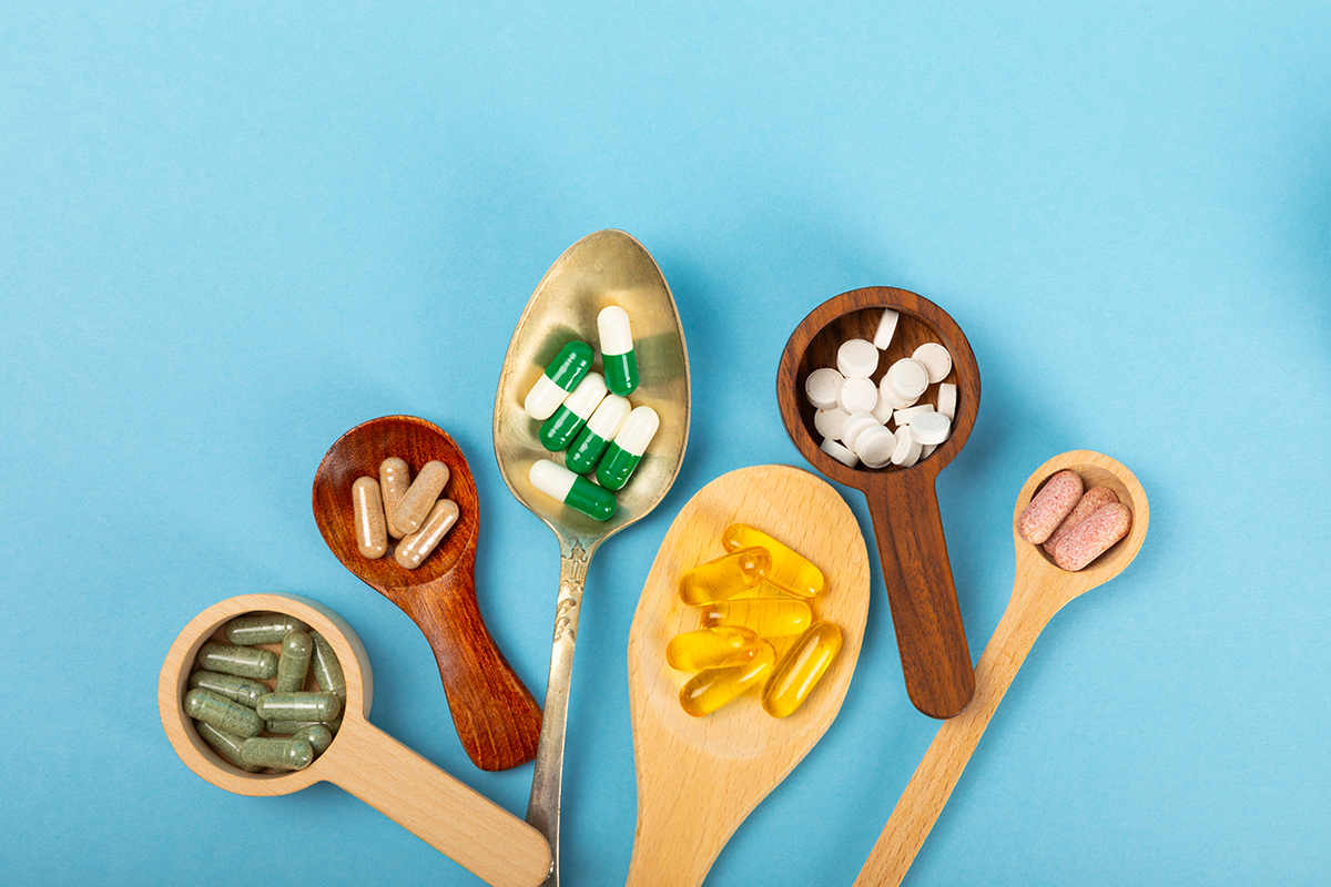 A selection of wooden spoons and a metal spoon, all containing vitamins, are set against a blue background.