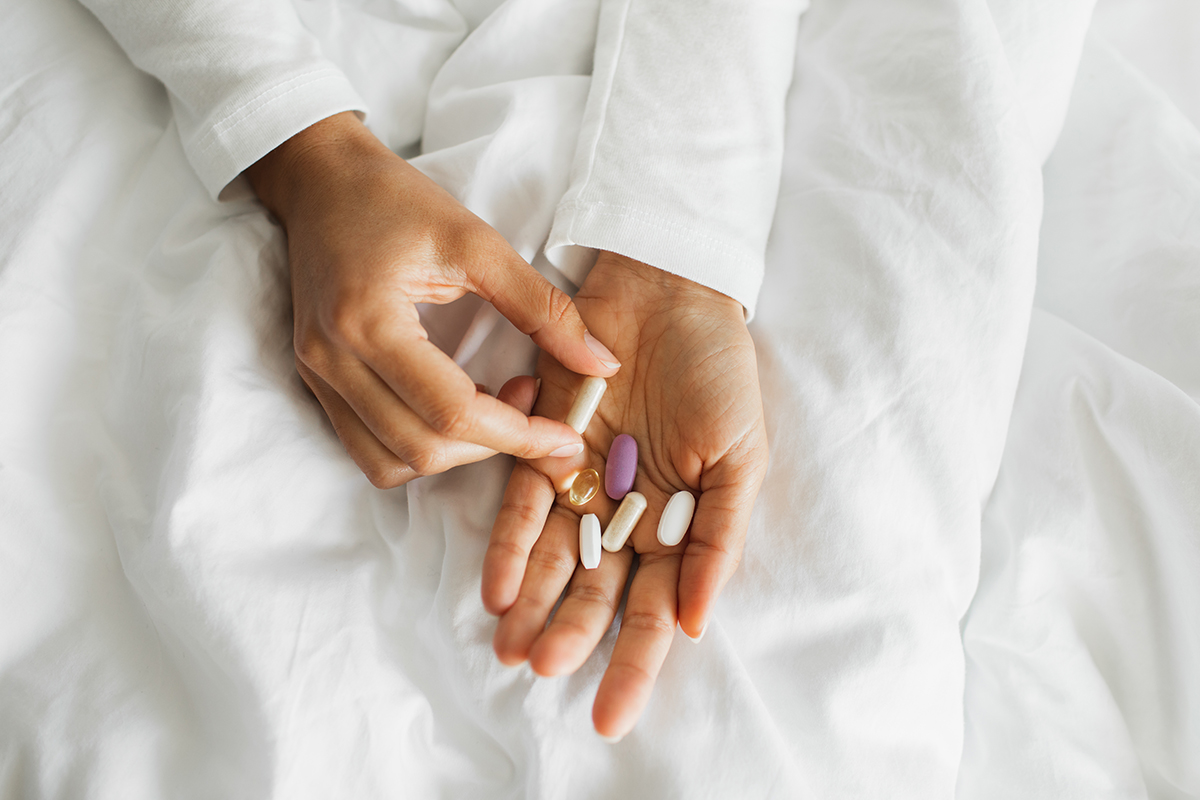 A close up of hands on top of white bedding holding a selection of vitamins.