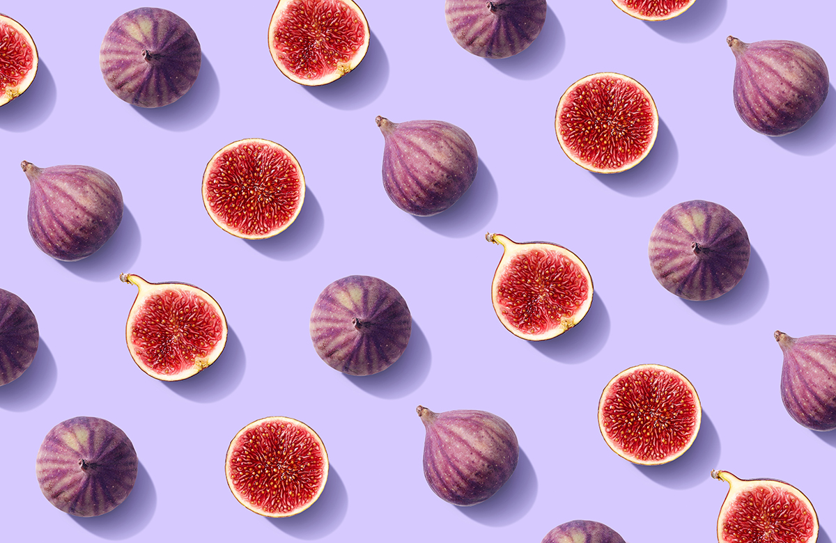 A pattern of whole and halved fresh figs are arranged on a purple background.