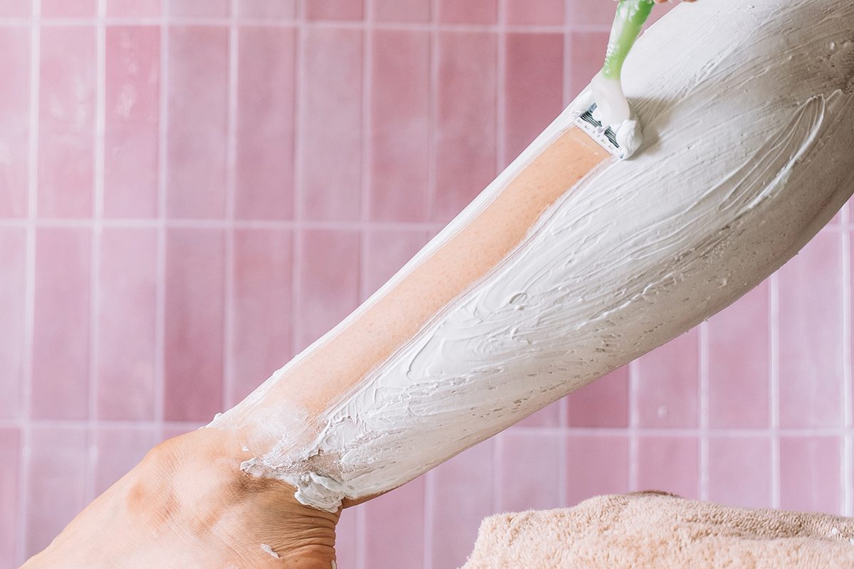 A close-up of a person shaving their leg in a pink bathroom