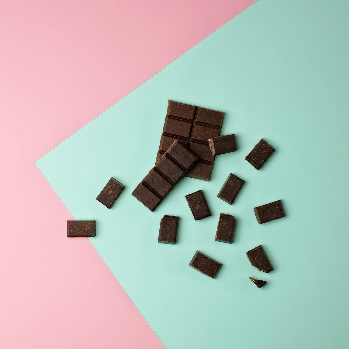 Dark chocolate bar pieces on a pink and mint green color blocked background.