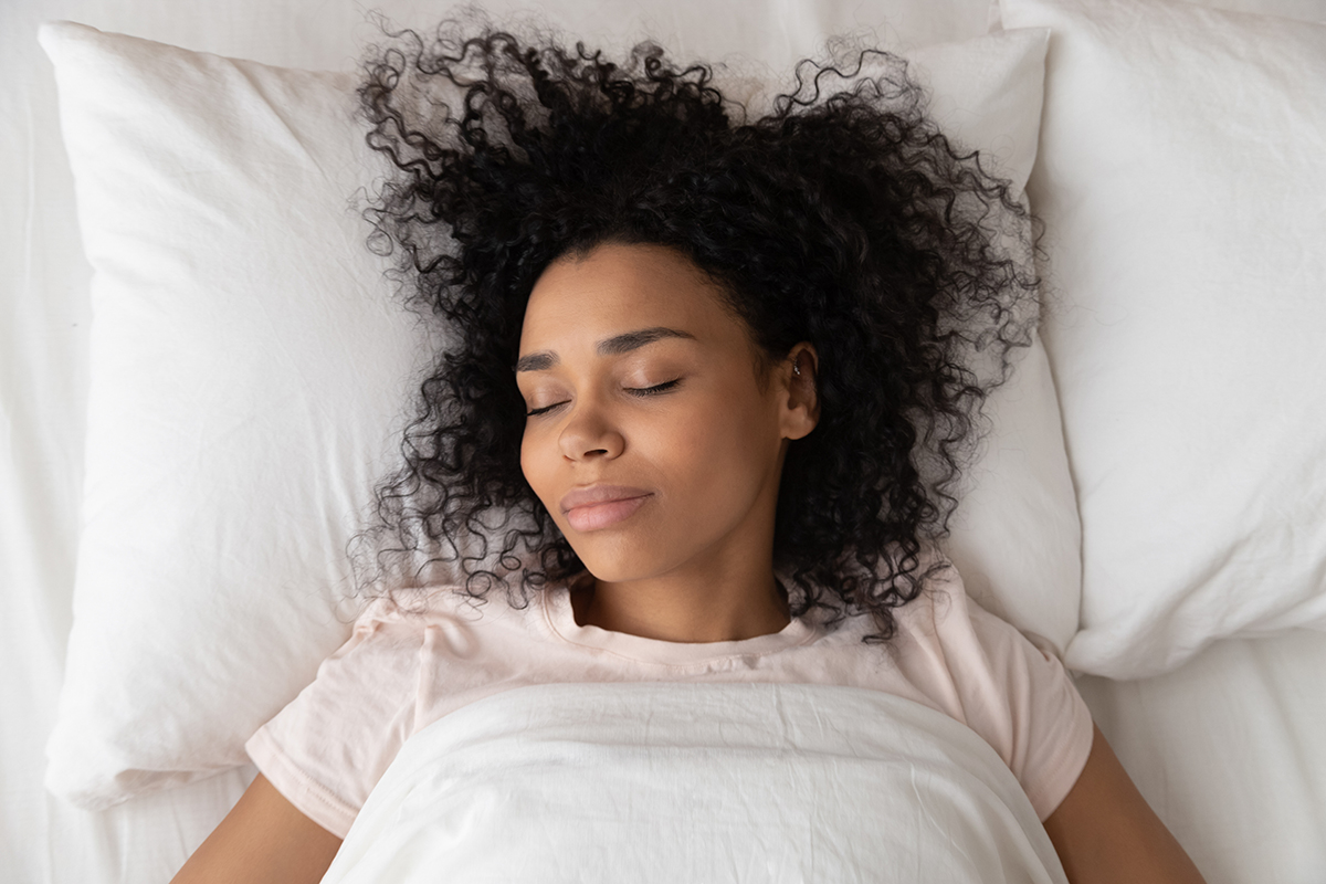 A woman sleeps on her back in a bed with white bedding.