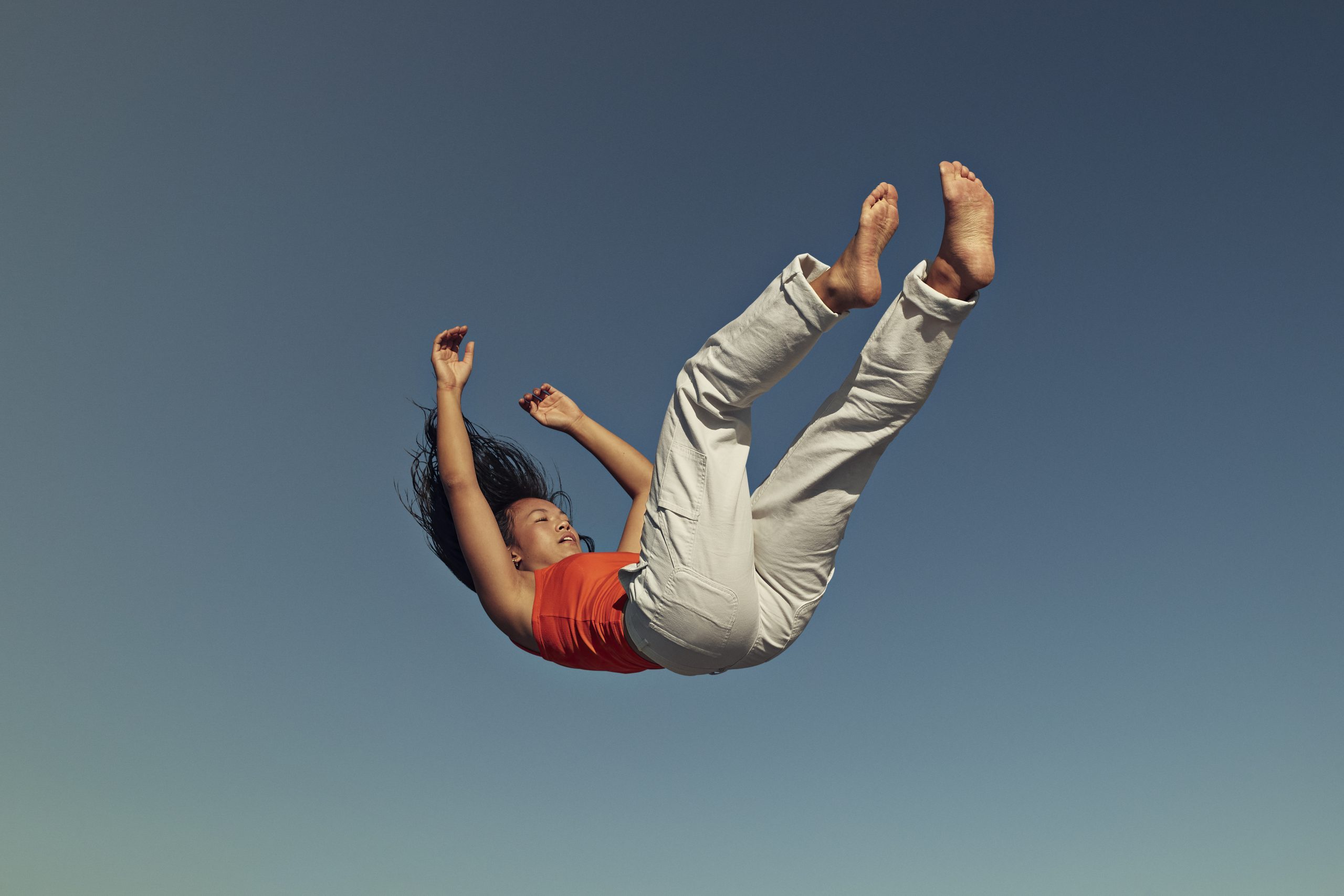 Side view of young woman falling against clear blue sky