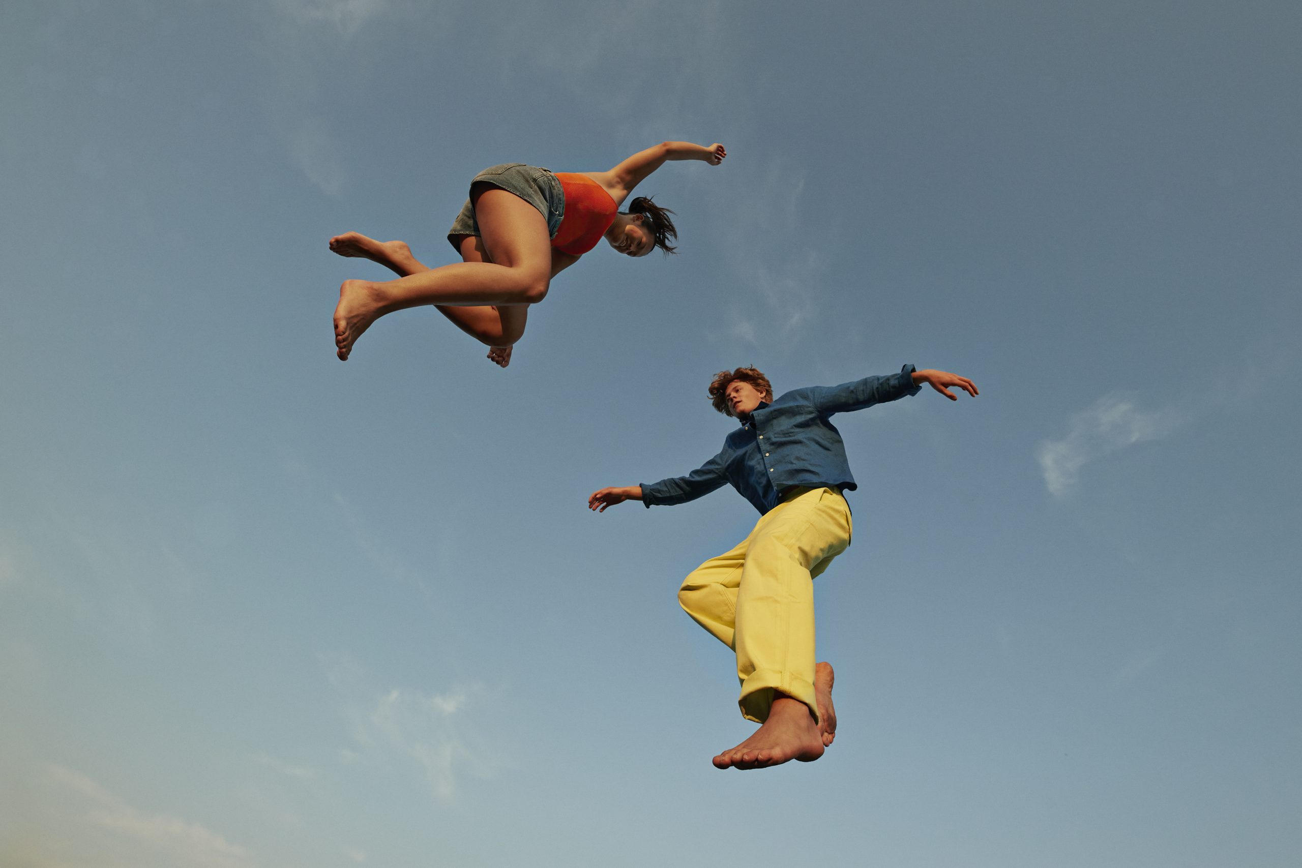 Woman jumping with male friend against sky