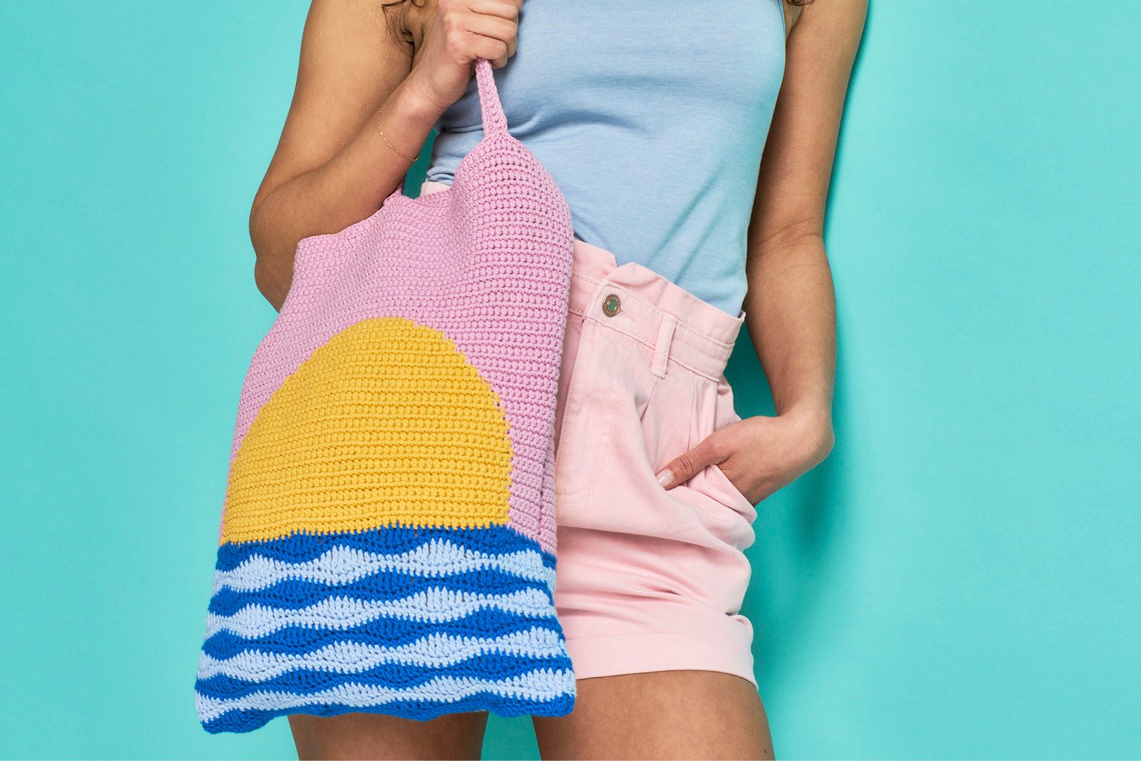 Crochet tote bag depicting a sun rising above the water in a pink sky