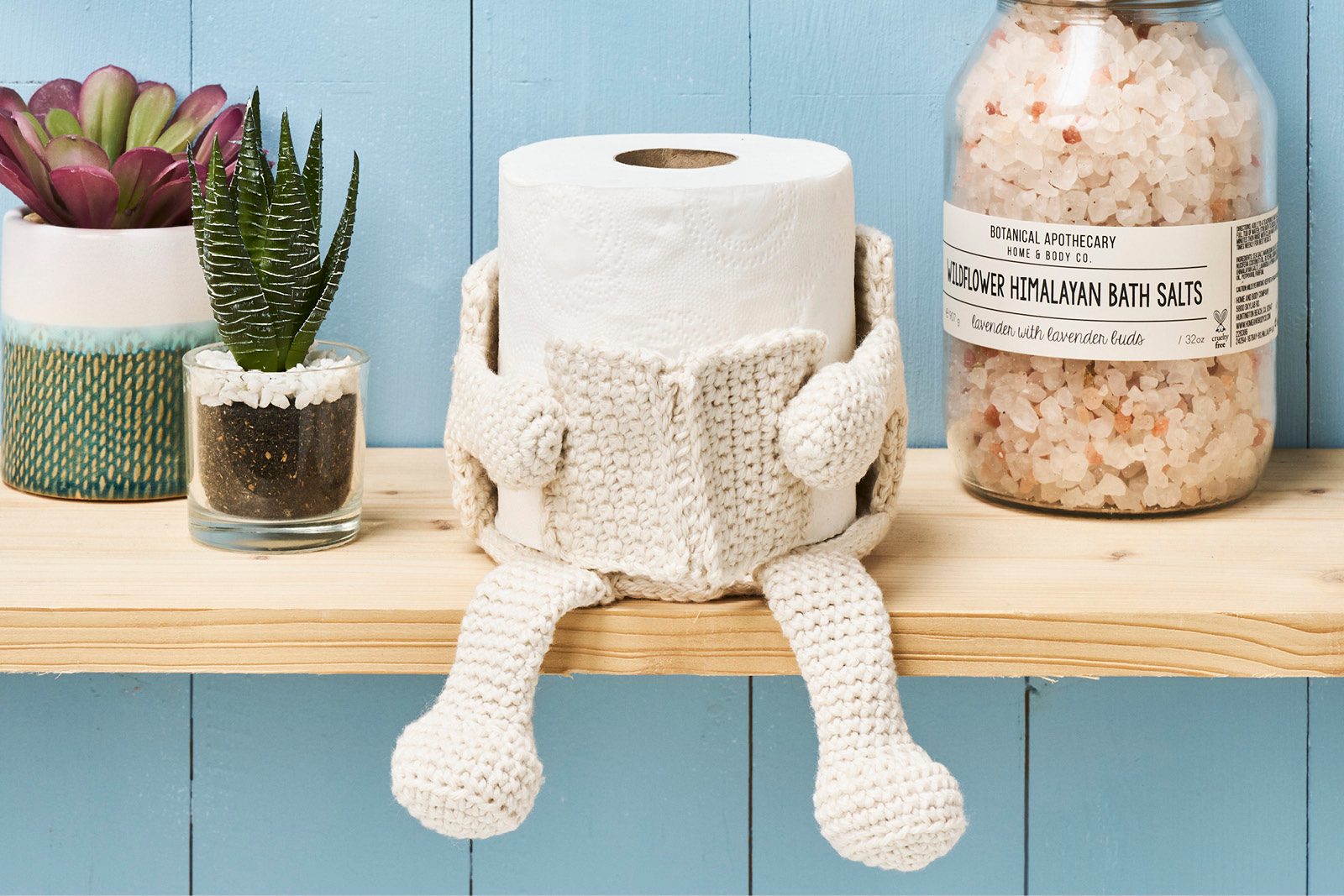 Loo roll with crochet arms and legs reading a crochet book