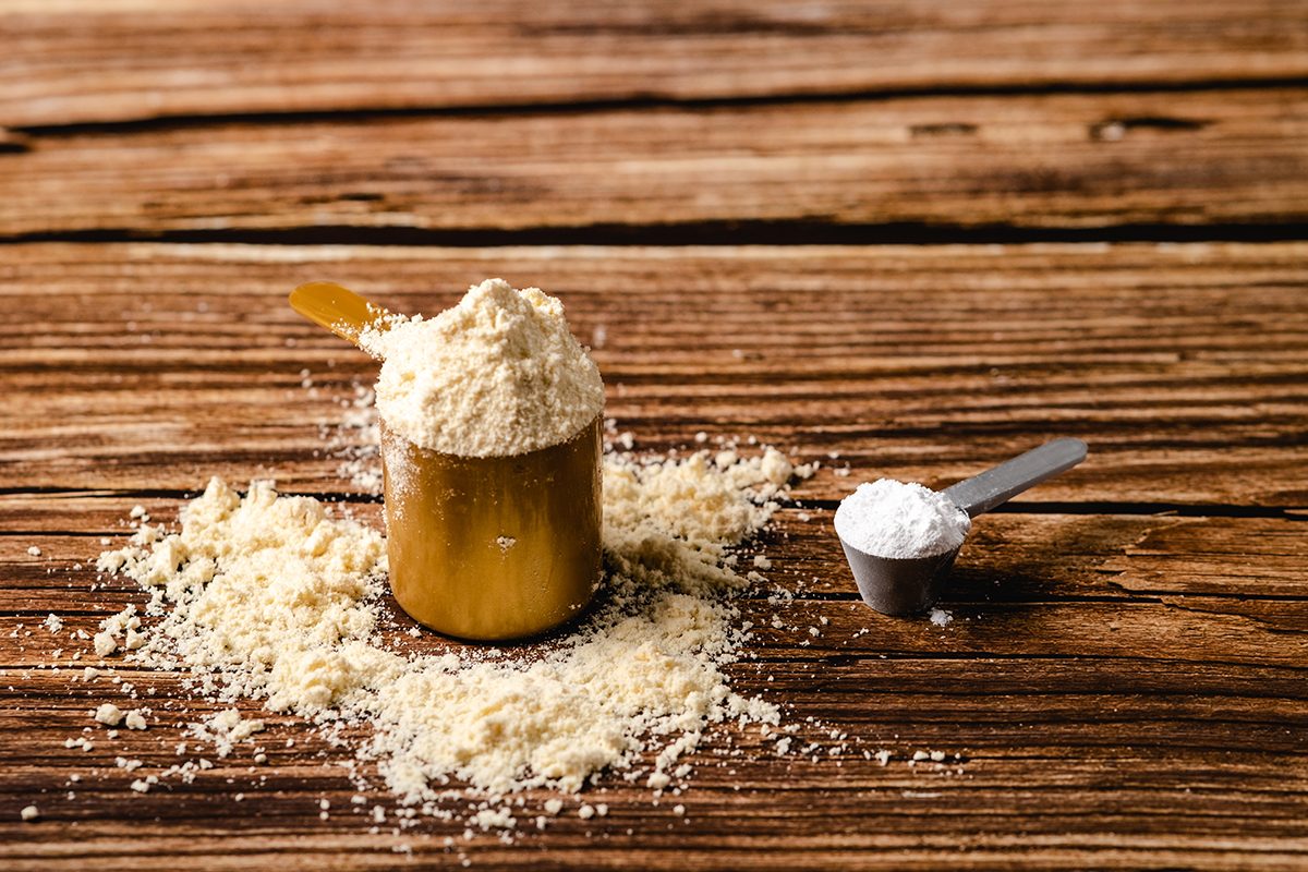 A large and a small scoop filled with different sports supplements on a wooden surface