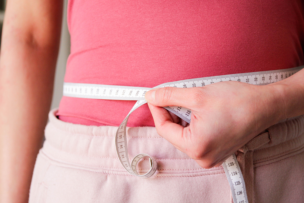 A woman measuring her waist with a measuring tape