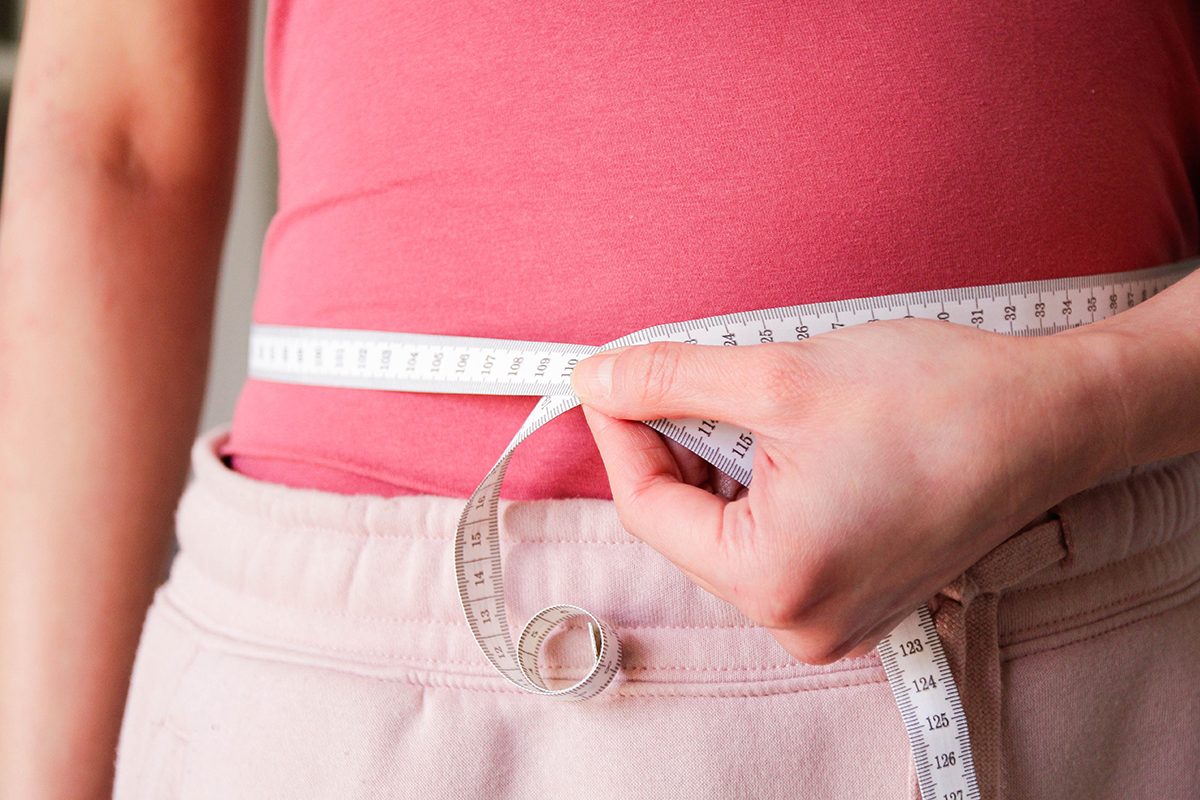 A woman measuring her waist with a measuring tape