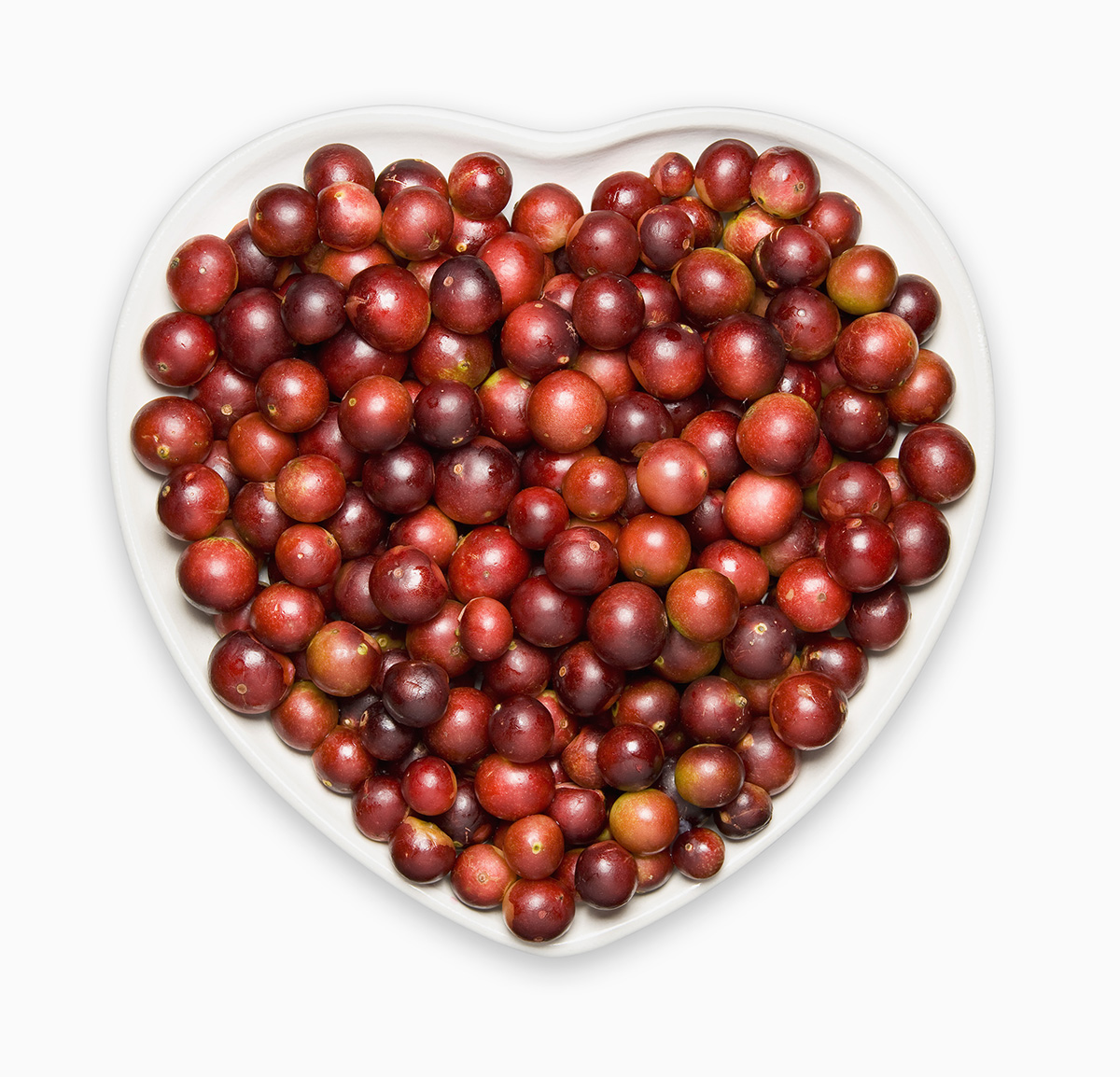 A heart-shaped plate covered in red-coloured camu camu berries is set against a white background.