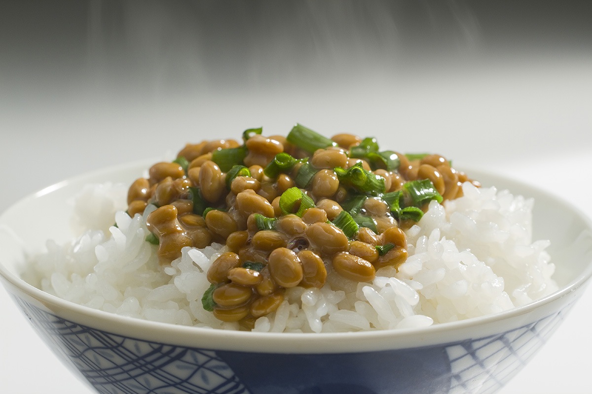 Steam rises from a white bowl containing white rice and natto.