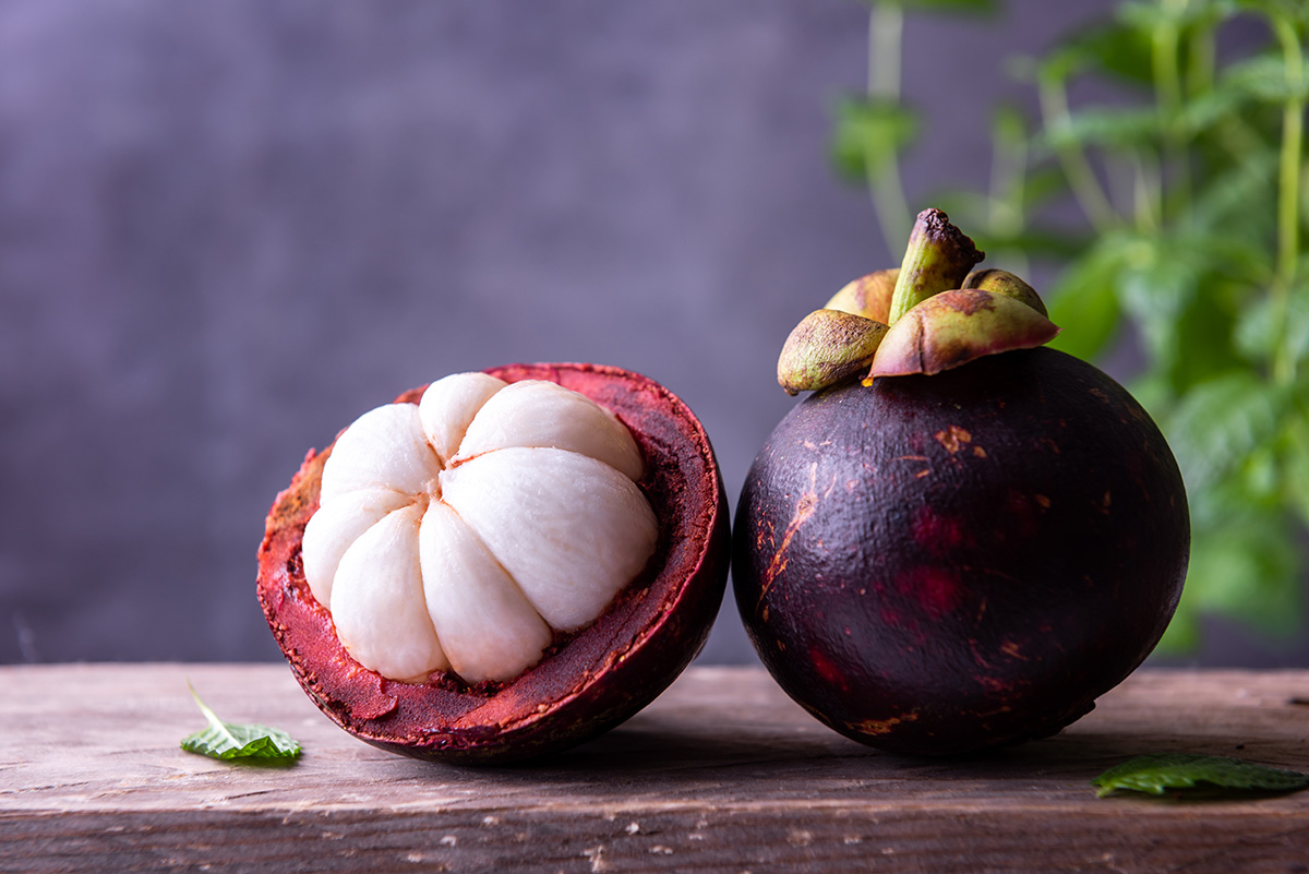 A whole mangosteen and a halved one sit on a wooden surface.