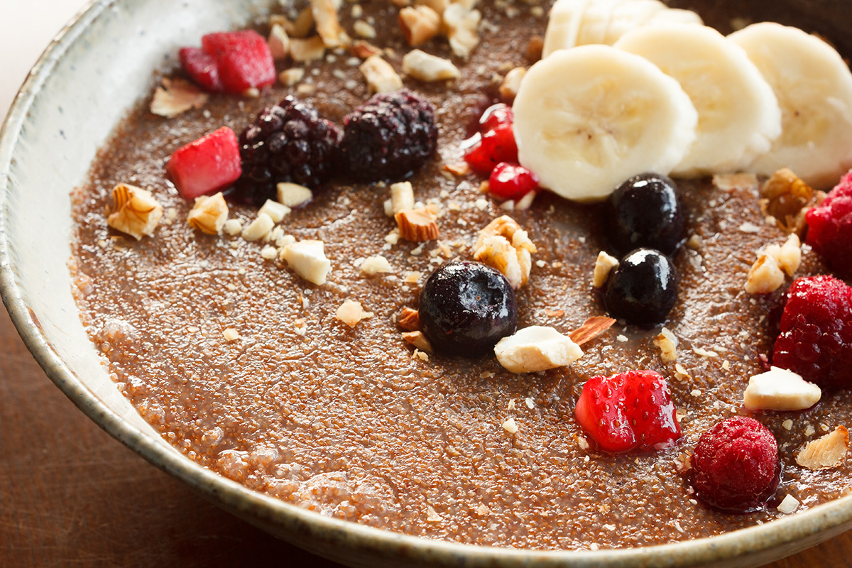 A bowl of porridge made from teff and topped with banana slices, nuts and berries is shown.