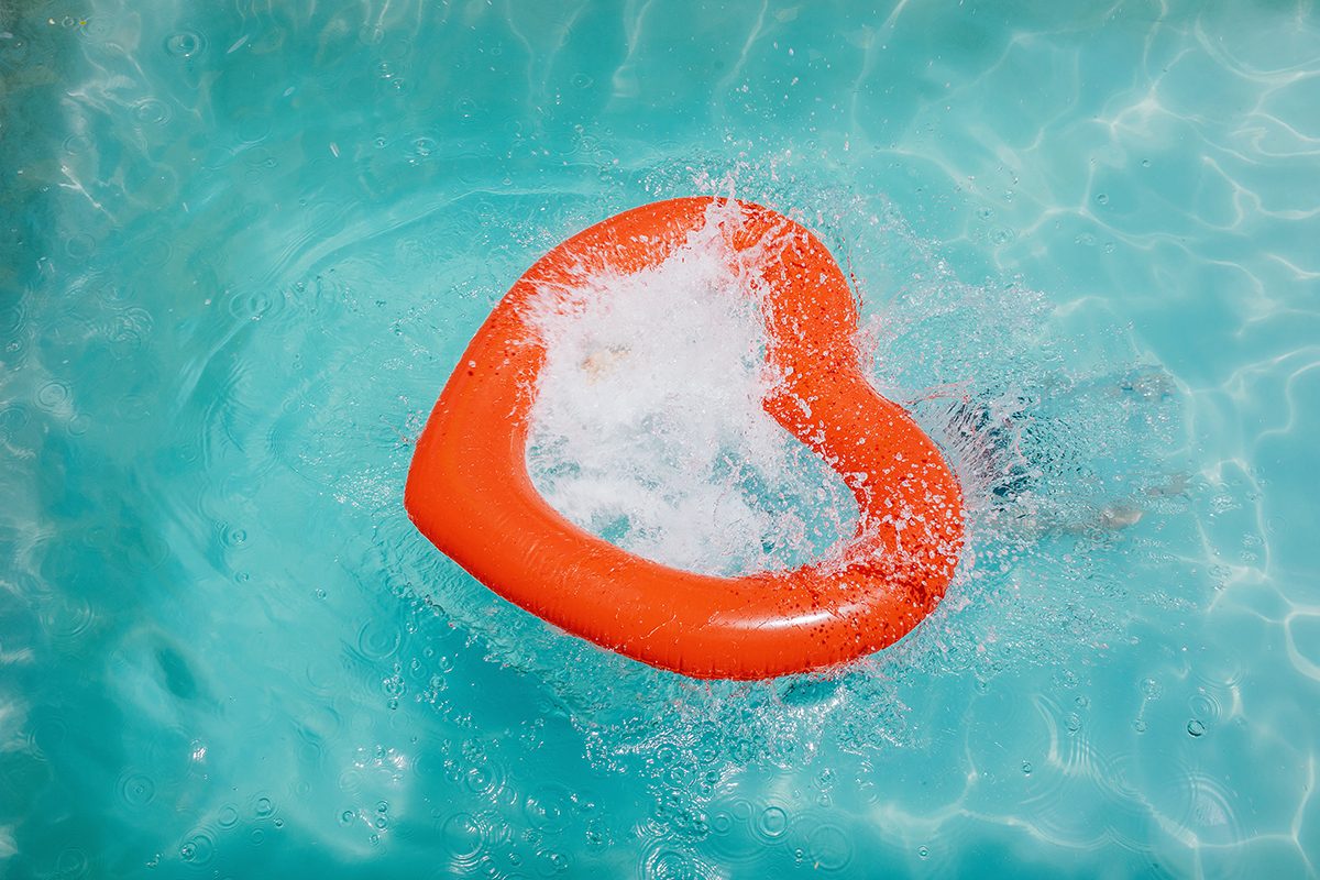A person is swimming underwater, below a heart-shaped inflatable, in a pool