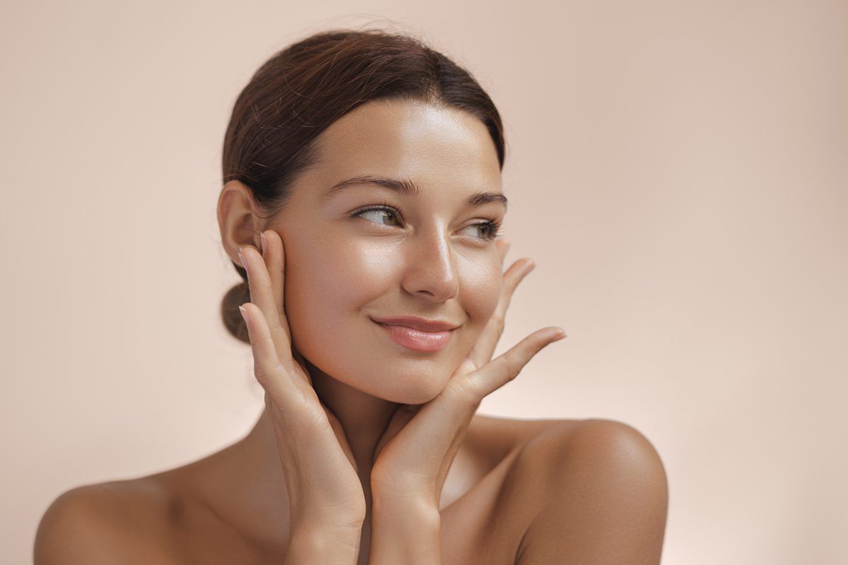 A portrait of a young woman with clear skin touching her face with both hands
