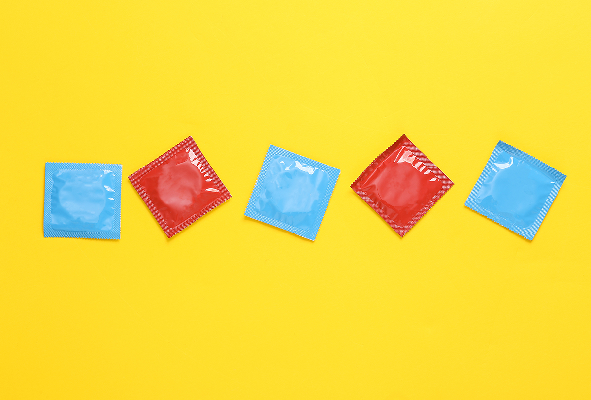 Condoms in blue and red packets are arranged in a line on a yellow background