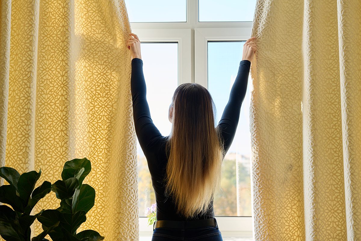 A woman is closing thick yellow curtains