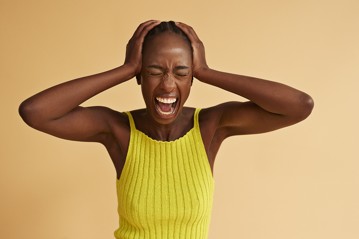 A woman screaming with her hands on her head against a beige background