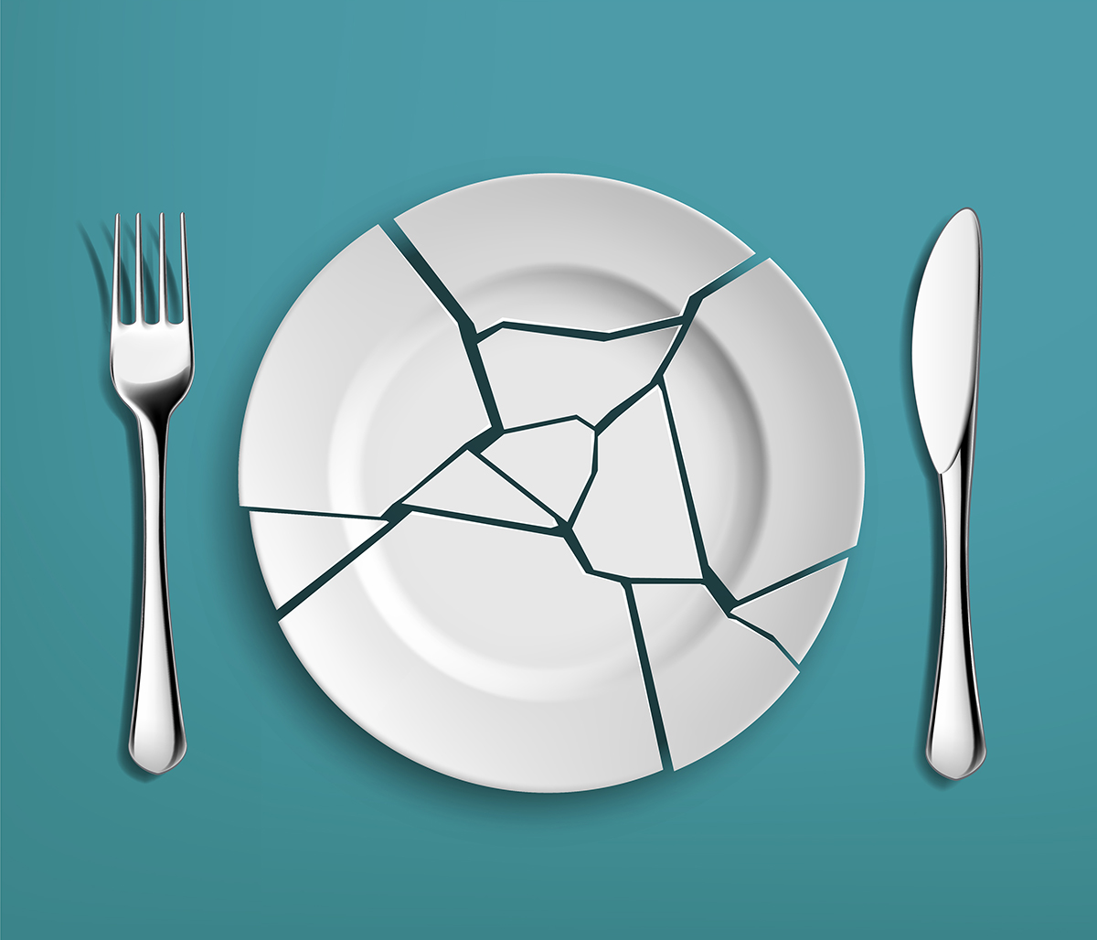 A white broken plate in between a knife and fork on a blue background