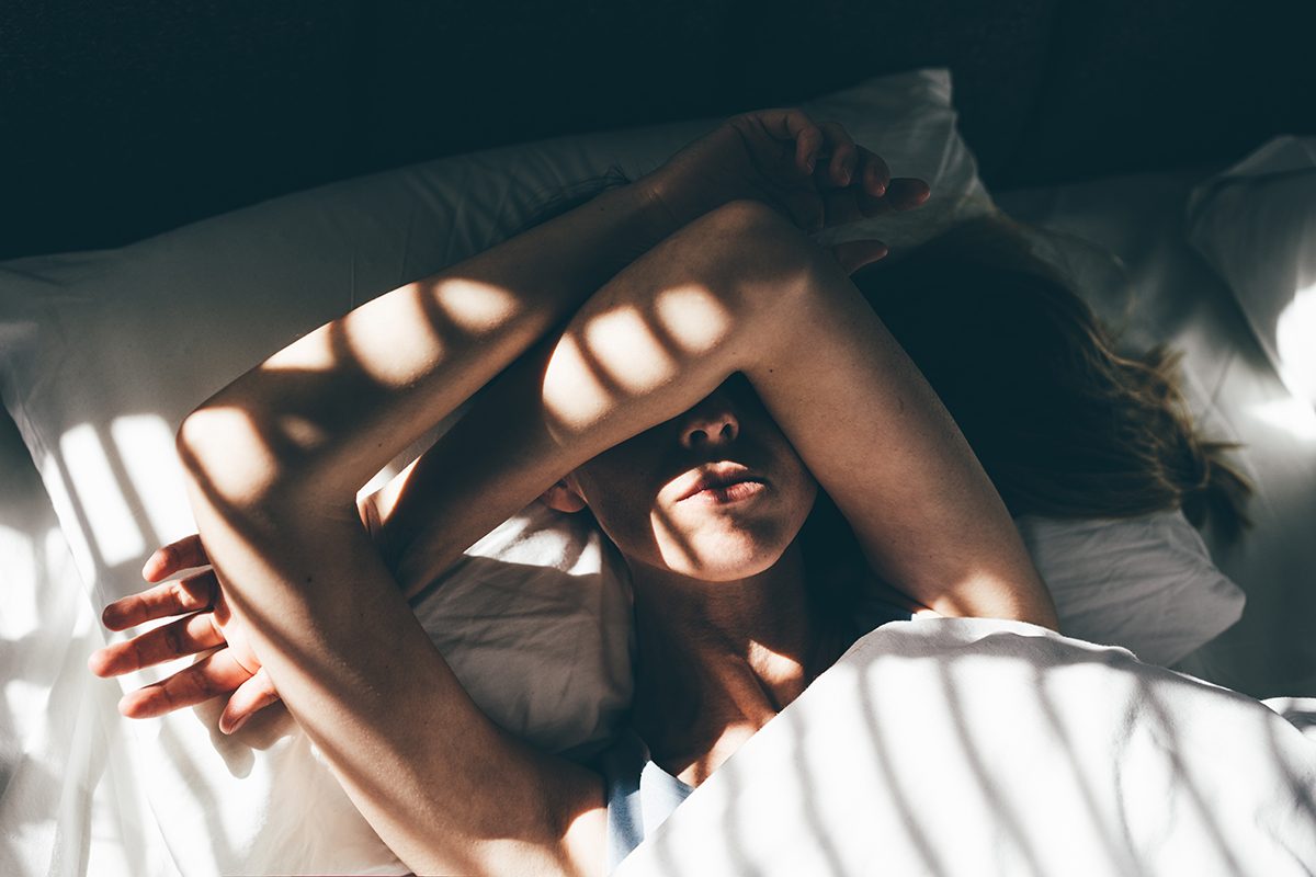 A woman lying in a bed with her arms covering her face