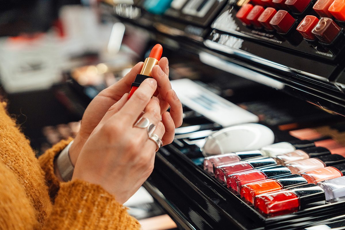 Female hands hold a red lipstick at a beauty counter