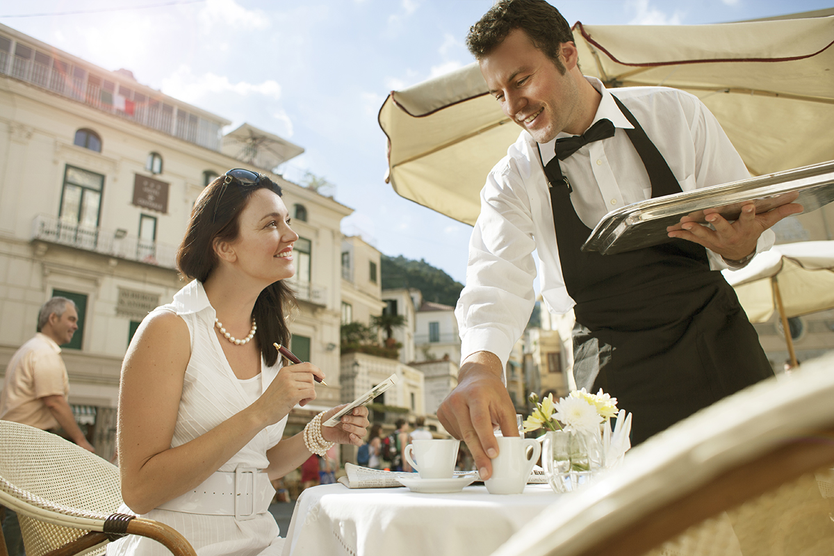 A woman being served by a waiter outside at a café