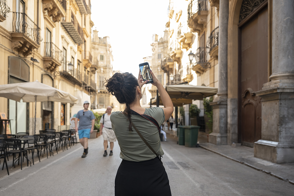 A woman taking a photo of a Mediterranean town on a smart phone
