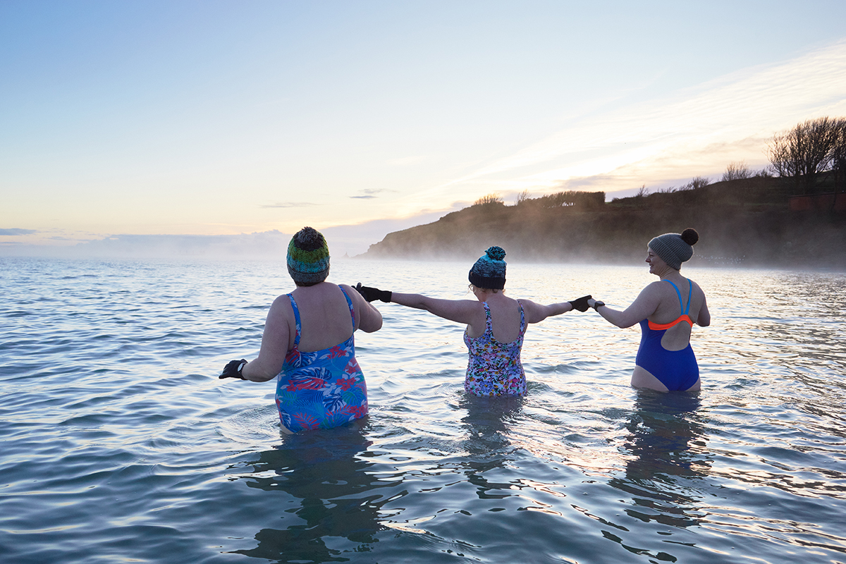 Three women wearing beanie hats wading in the sea