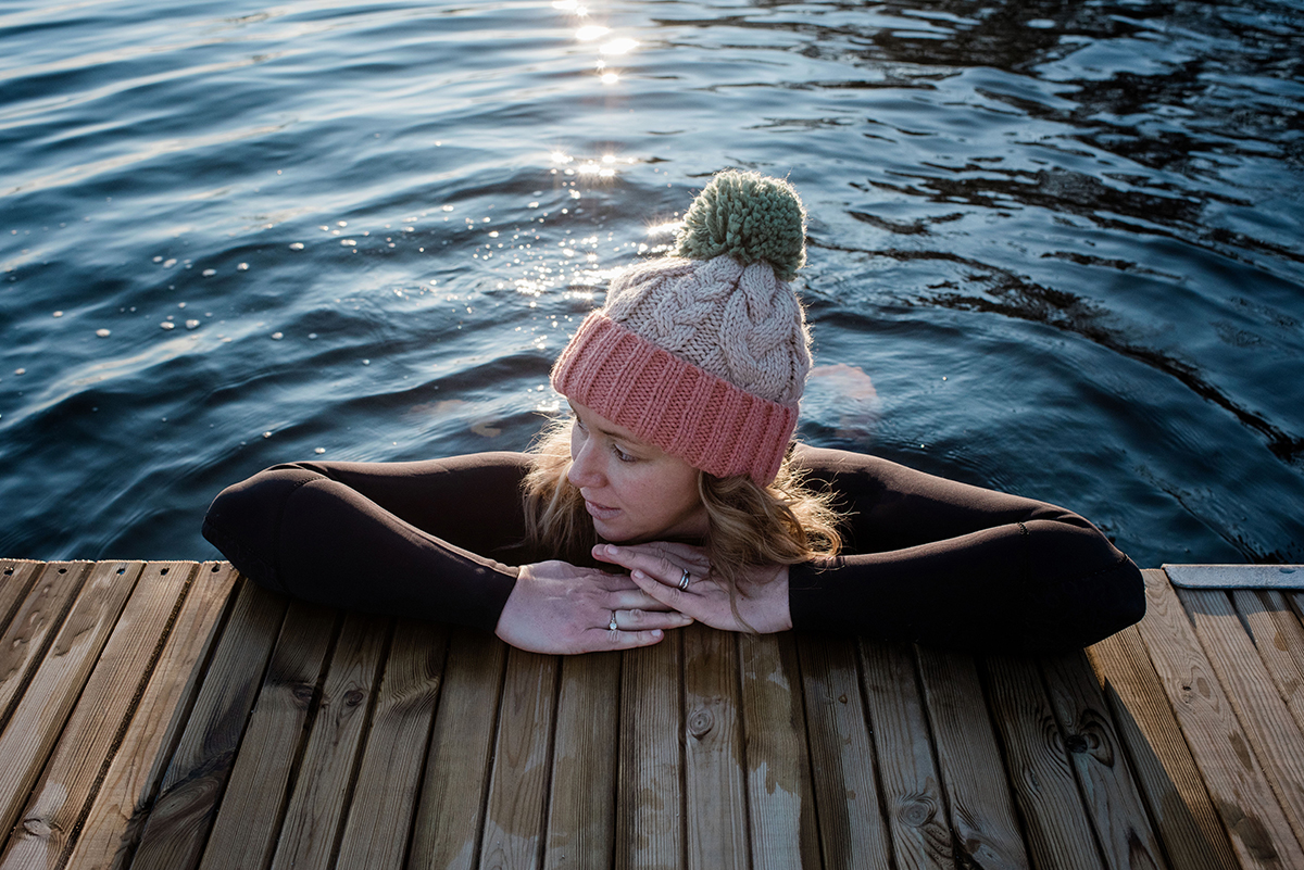 A woman wearing a beanie hat is leaning on a pier in cold sea water