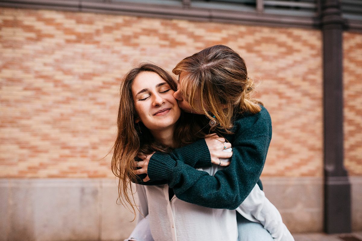A woman kisses her girlfriend on the cheek as she's carried on her back