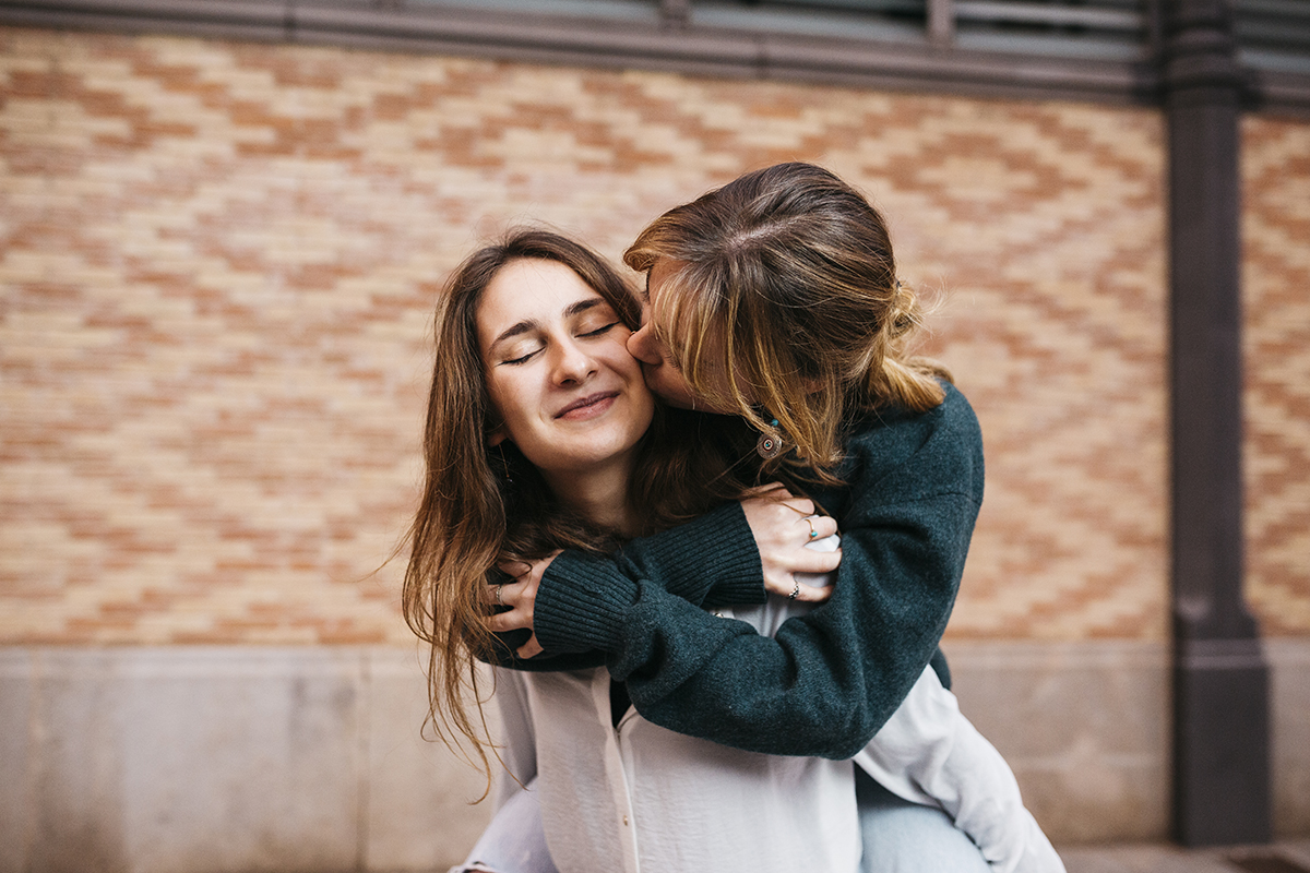 A woman kisses her girlfriend on the cheek as she's carried on her back