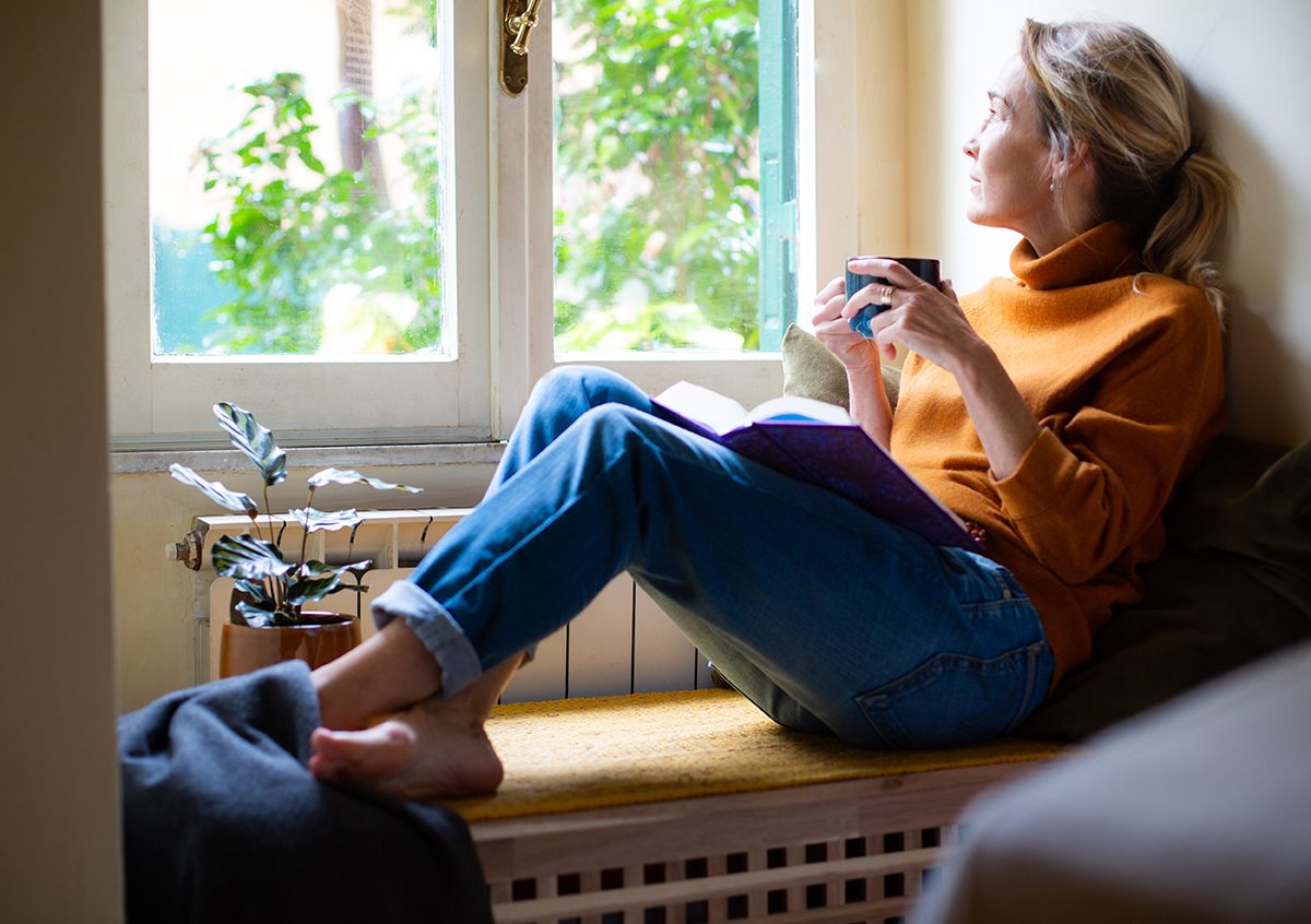 A woman looking out the window holding a cup of tea