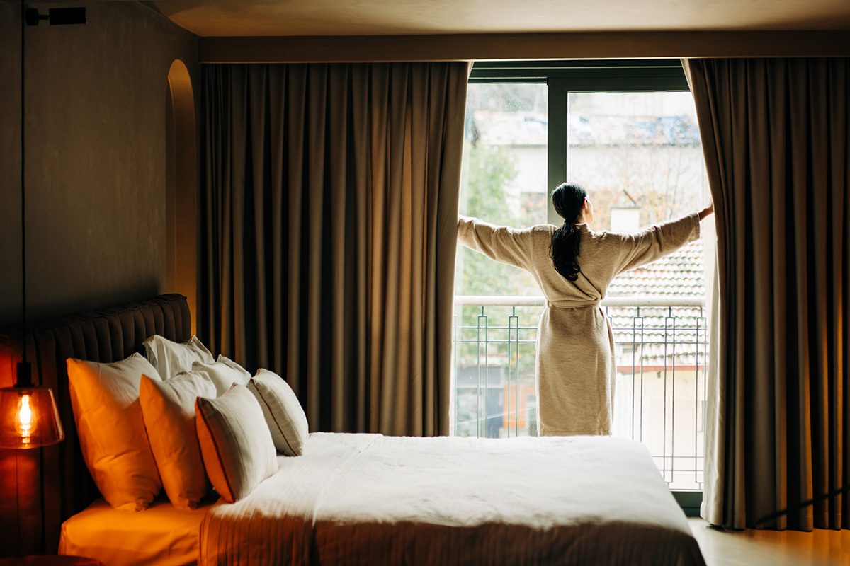 A woman wearing a robe is opening the curtains