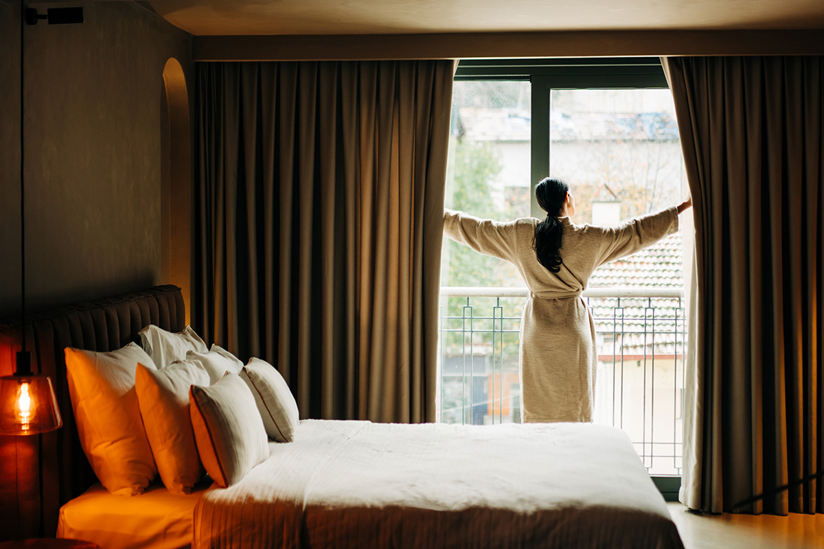A woman wearing a robe is opening the curtains