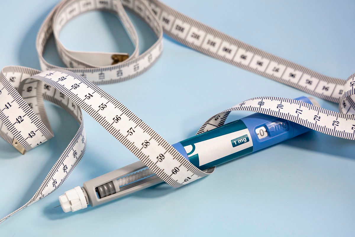 A measuring tape is wrapped around a GLP-1 pen on a blue background