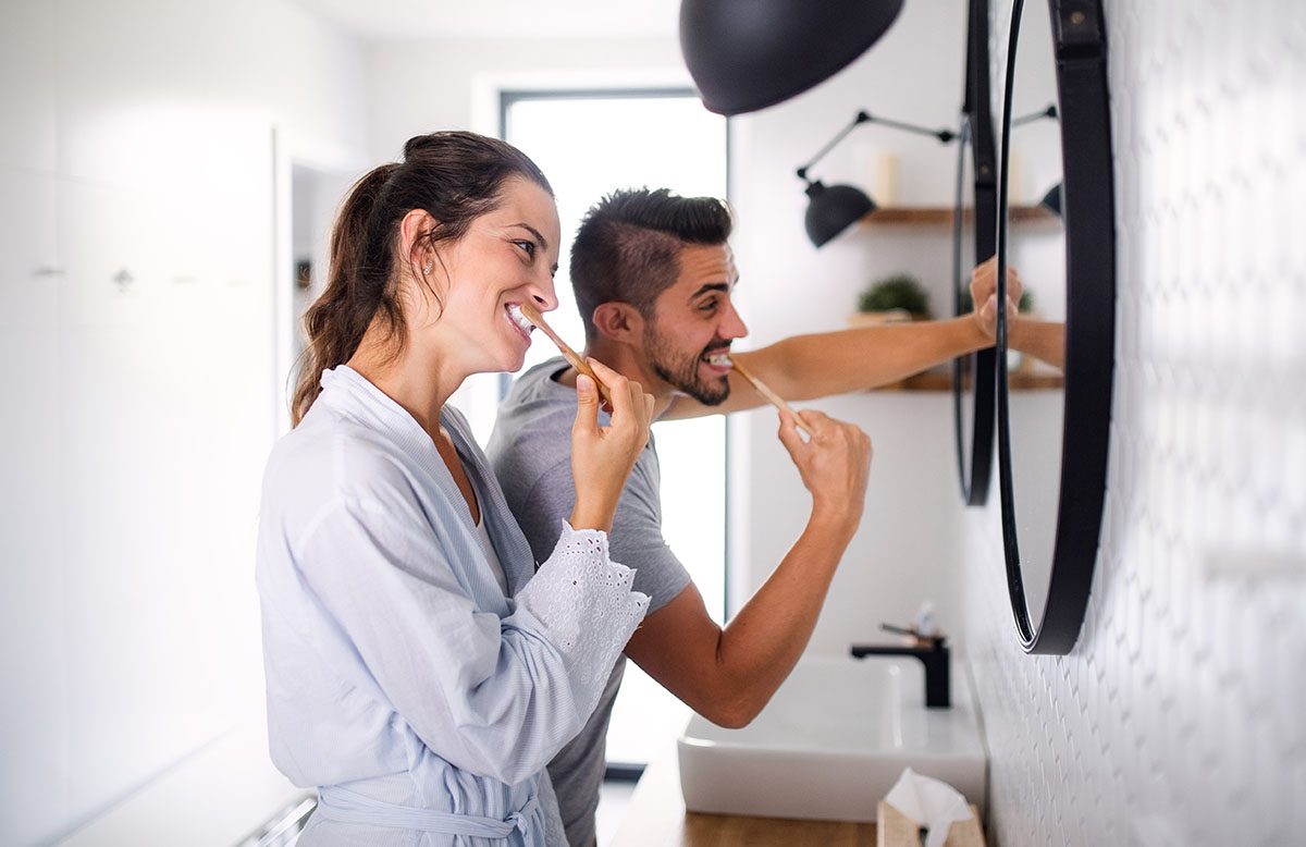 A man and a woman brushing their teeth in front of the mirror