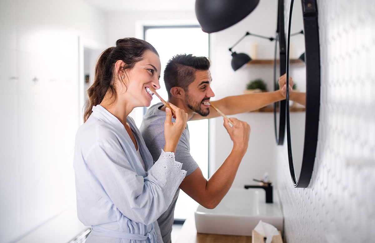 A man and a woman brushing their teeth in front of the mirror