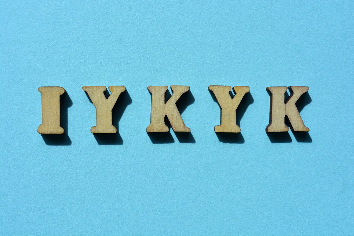 "IYKYK", the acronym for "If You Know You Know", is written in wooden letters and displayed on a blue background.