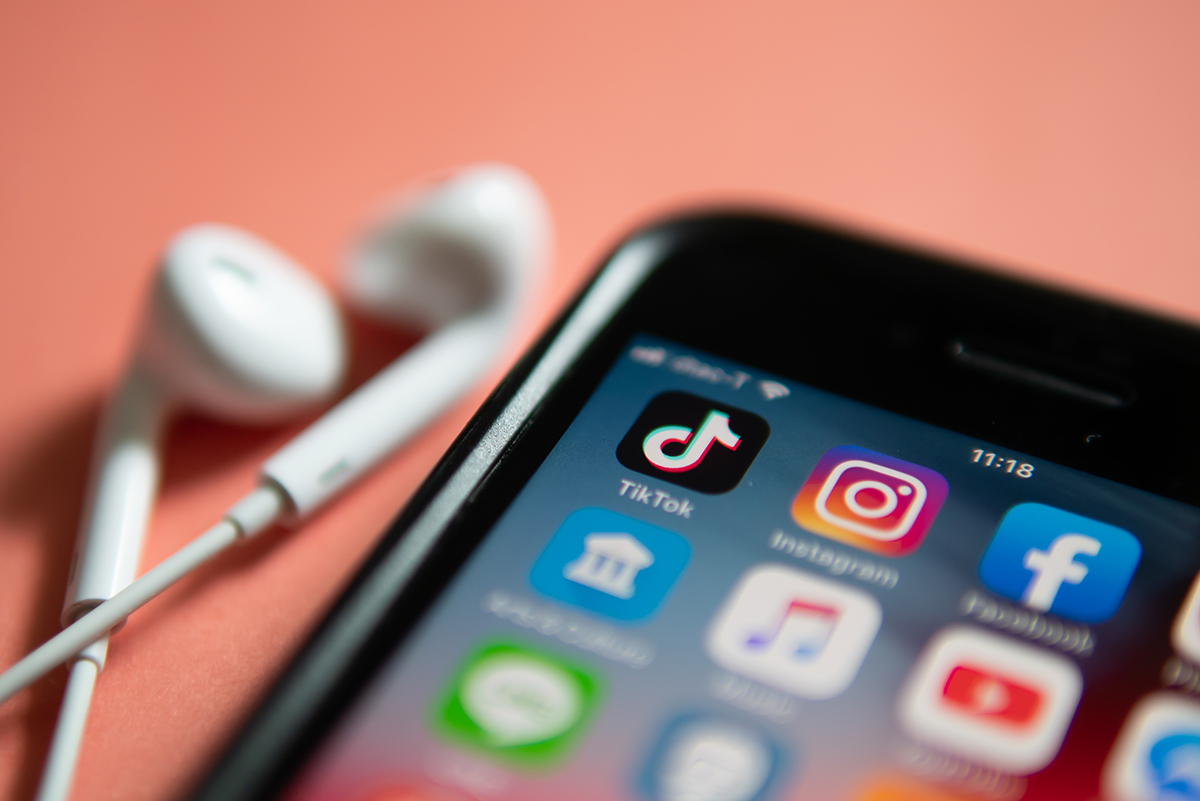 The corner of an iPhone and wired headphones are shown on an orange background. On the phone screen you can see a selection of apps, including TikTok, Instagram, Facebook and YouTube.