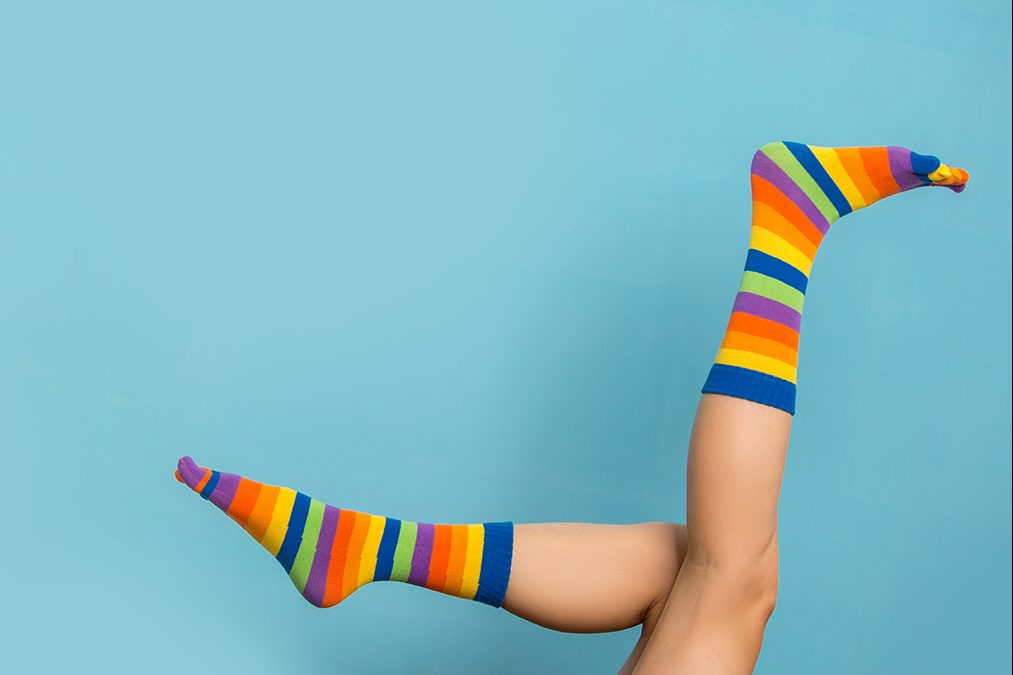 Legs wearing colourful, striped knee-high socks are playfully kicking in the air against a light blue background.
