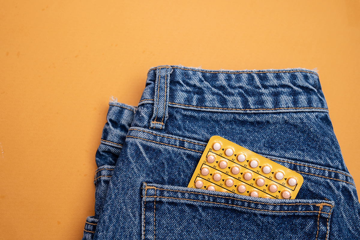 A pack of contraceptive pills tucked into the pocket of a pair of jeans on an orange background