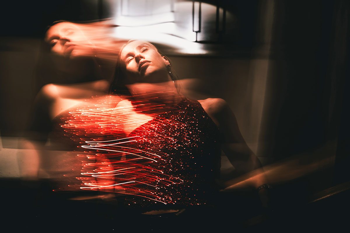 A blurred shot of a woman wearing a sparkly red dress moving in a dimly lit setting
