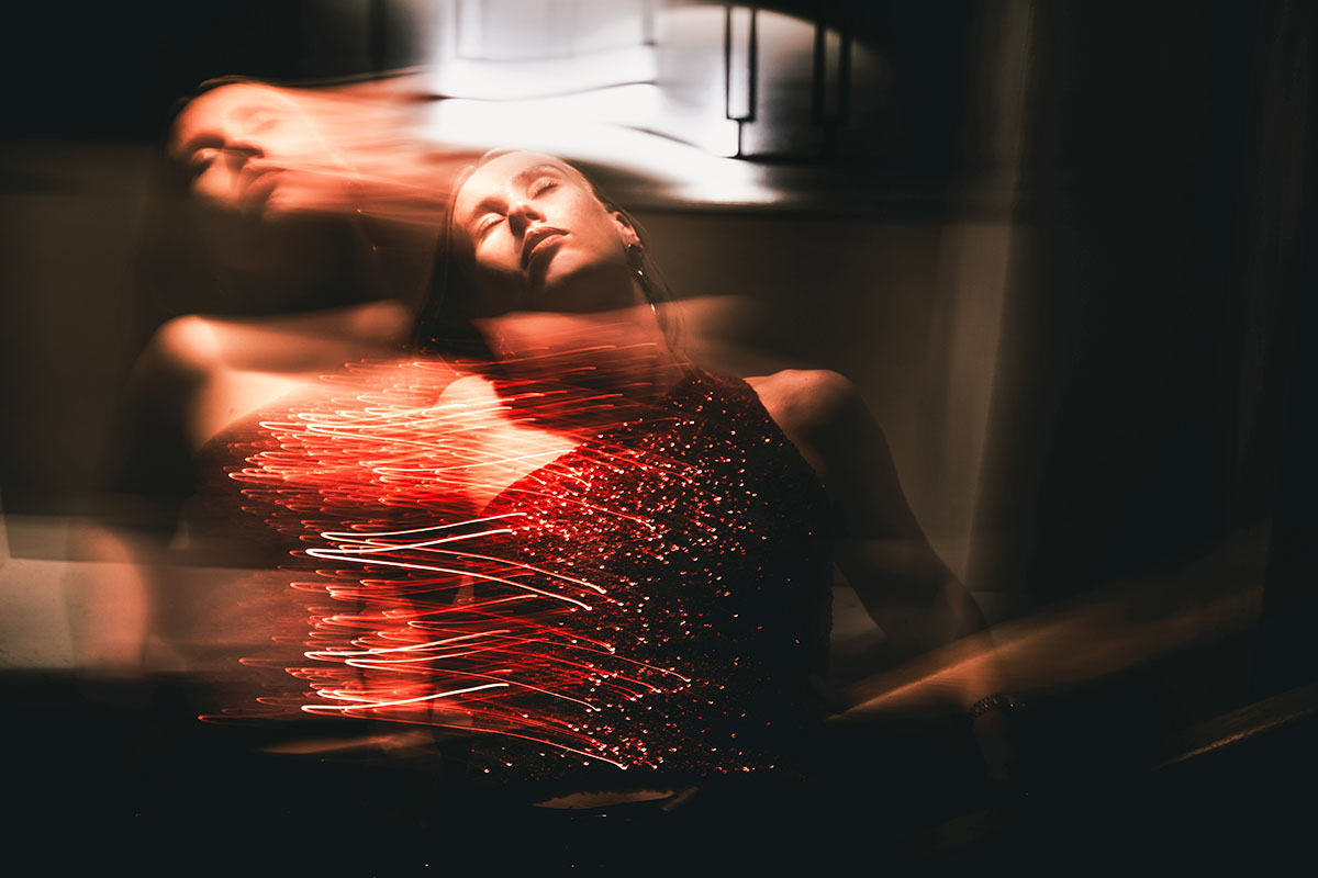 A blurred shot of a woman wearing a sparkly red dress moving in a dimly lit setting