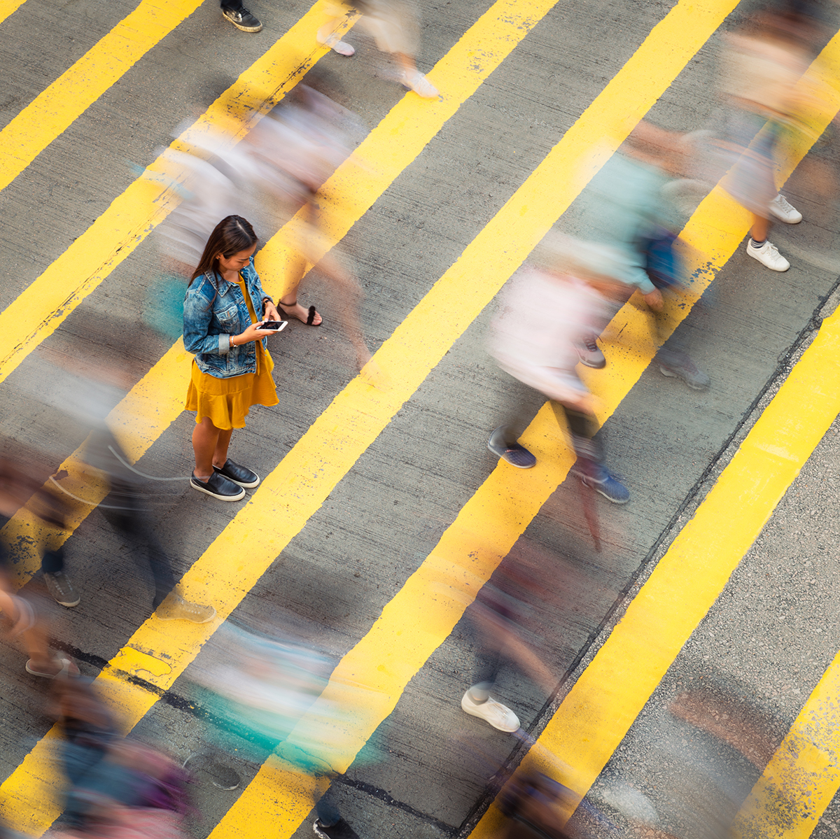A blurred image of a woman standing on a crossing and looking at her phone