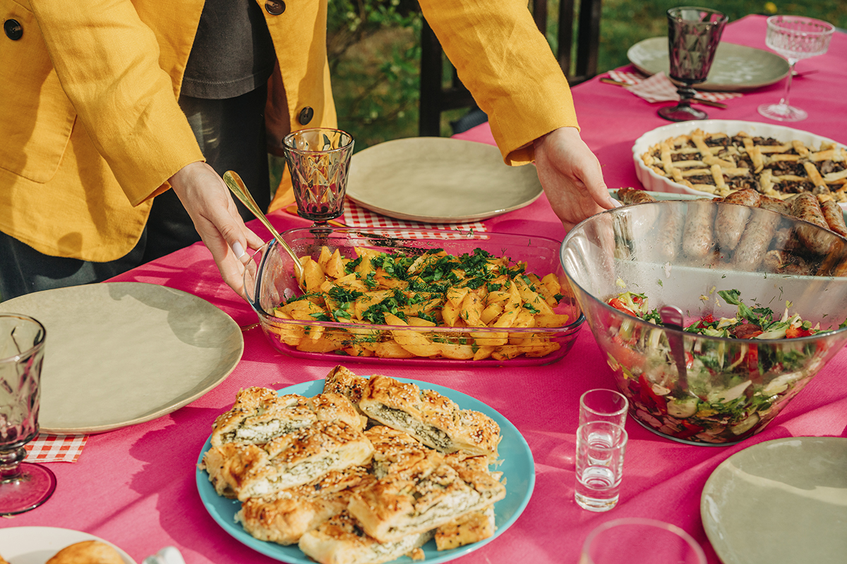 A woman placing a dish of cooked potato onto a dining table