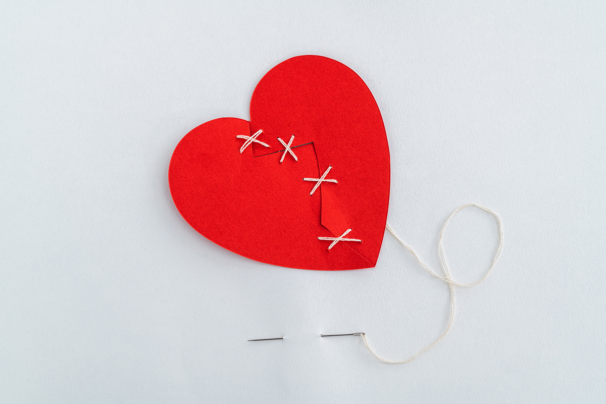 A broken red heart has been stitched back together with white thread