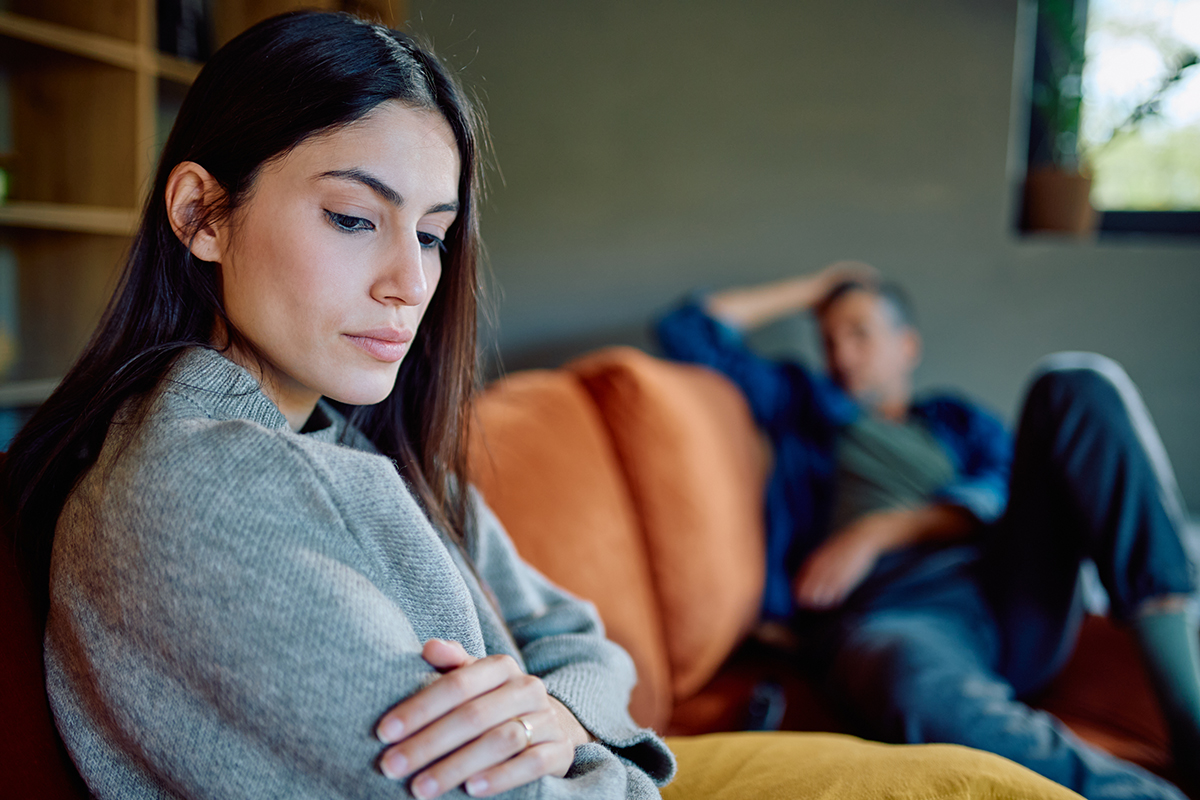 A couple sit on opposite ends of a sofa suggesting they have had an argument