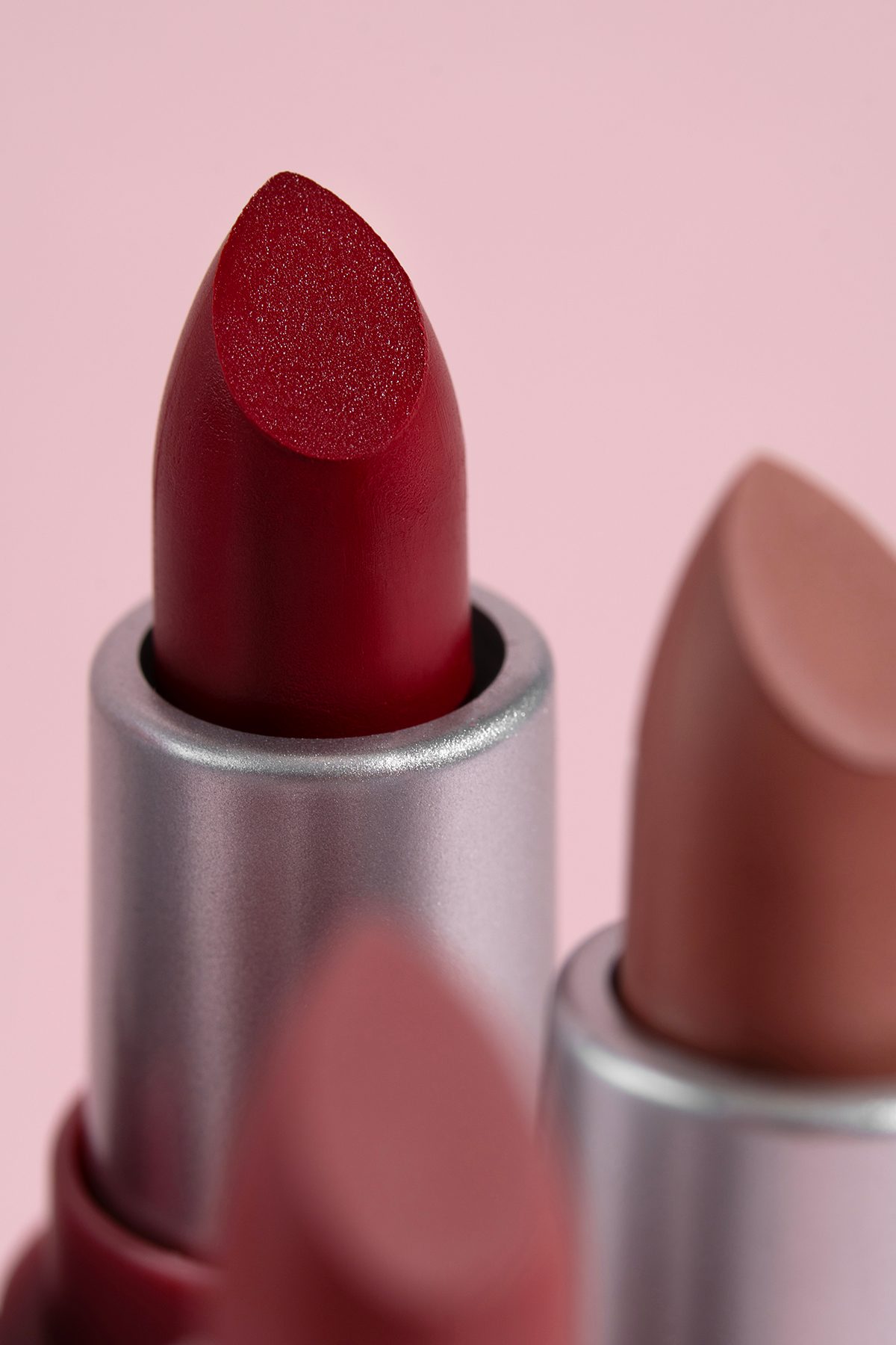A close-up of three lipsticks against a pink background