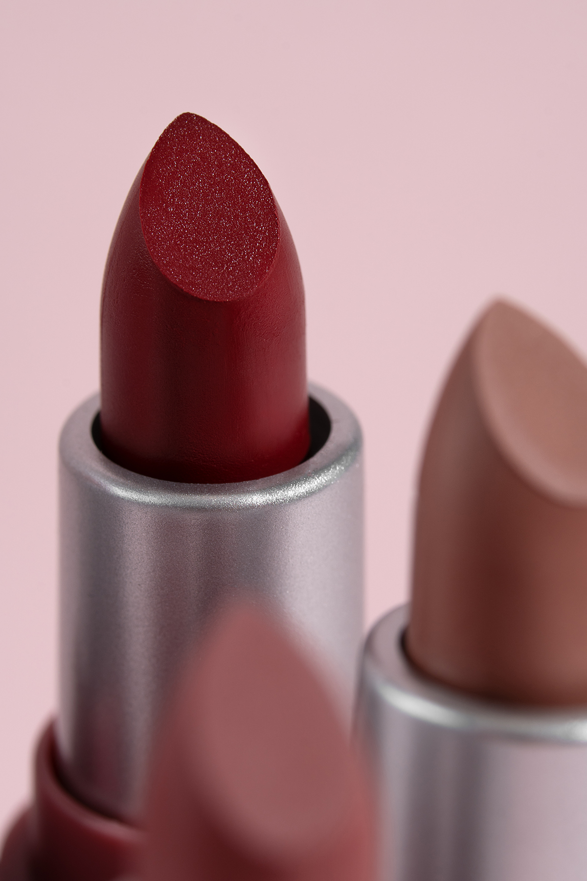 A close-up of three lipsticks against a pink background
